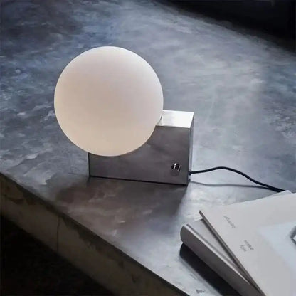 Dimmable LED desk light with a frosted glass ball and stainless steel base on a concrete surface. Ideal for modern home or office lighting.