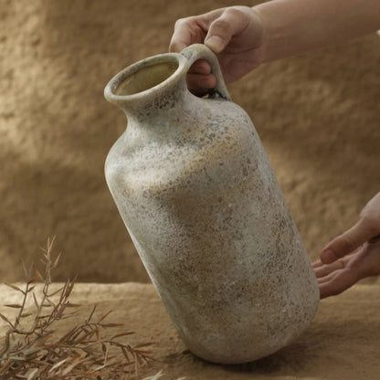 Person holding a rustic ceramic vase against a sandy background