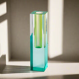 Tall, hexagonal glass candle holder with green and blue gradient on a light gray background