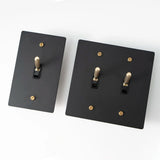 Two black light switch covers with gold screws on a white background