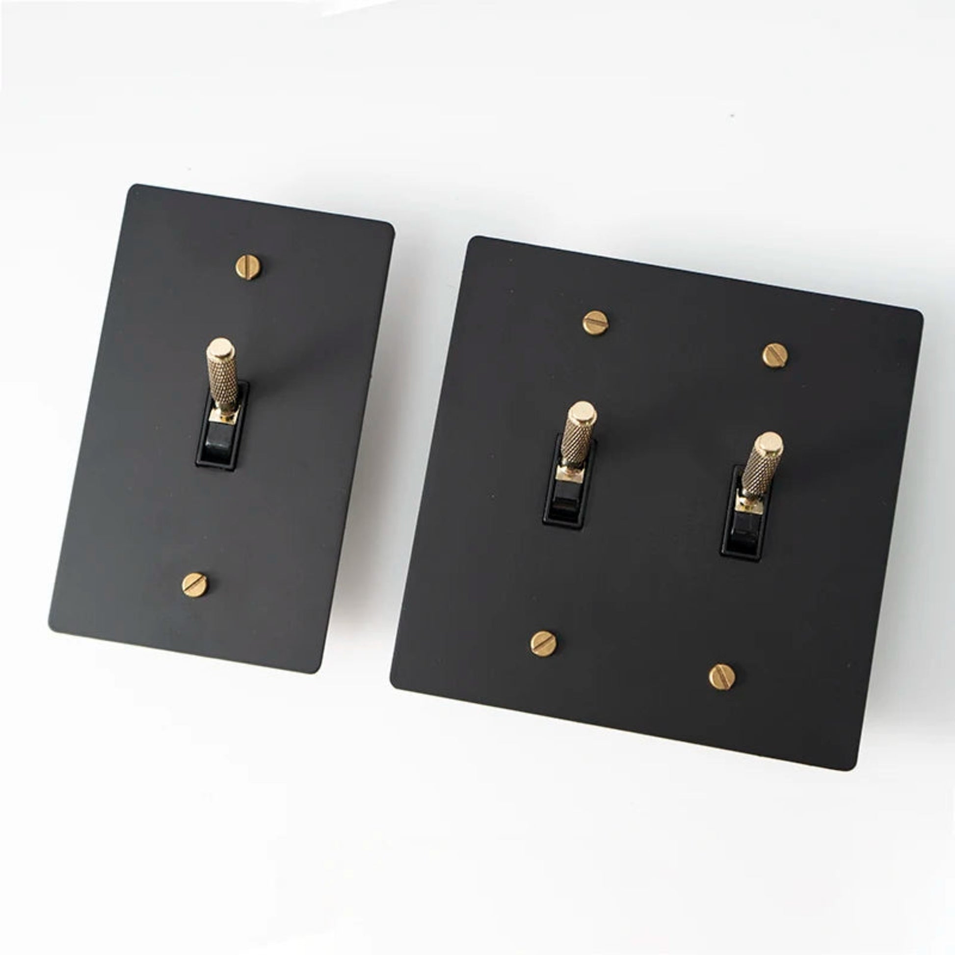 Two black light switch covers with gold screws on a white background