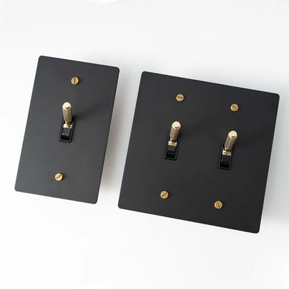 Two black light switch covers with gold screws on a white background