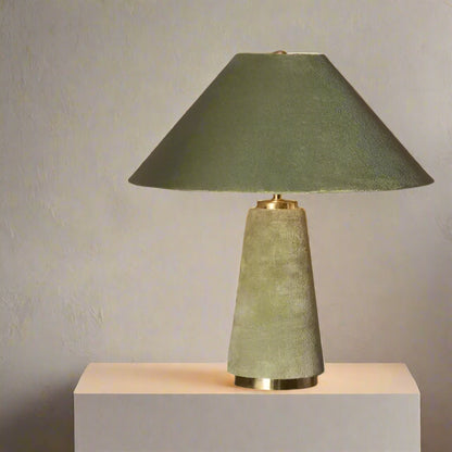Green table lamp with a textured base on a dark surface against a neutral background

