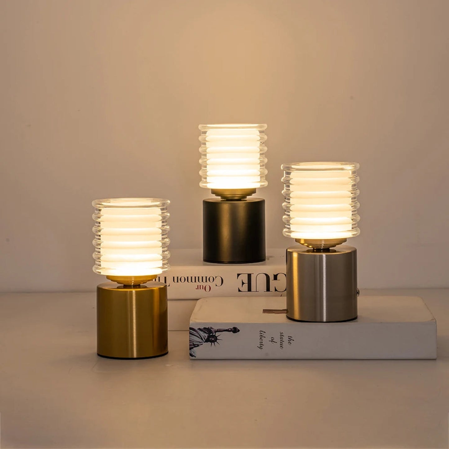 Three small table lamps with ribbed glass shades on books against a neutral background
