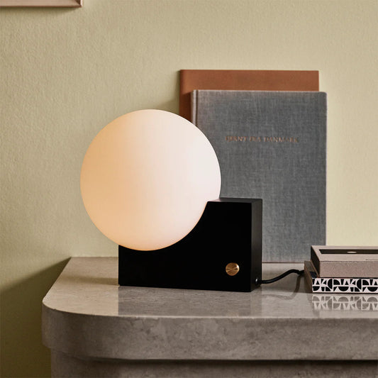 Modern table lamp with a spherical shade on a marble surface against a beige wall.

