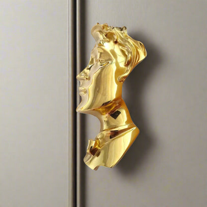 Gold-colored pendant with a face design on a white background