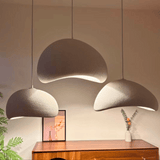 Three modern pendant lights hanging above a wooden cabinet with a plant and vase in the background.