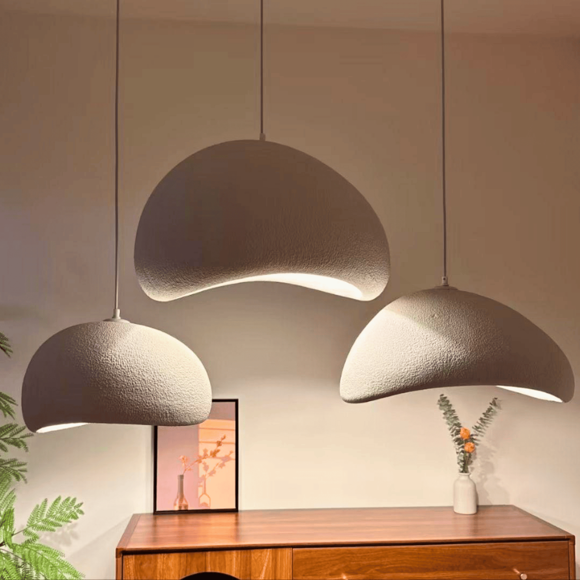 Three modern pendant lights hanging above a wooden cabinet with a plant and vase in the background.