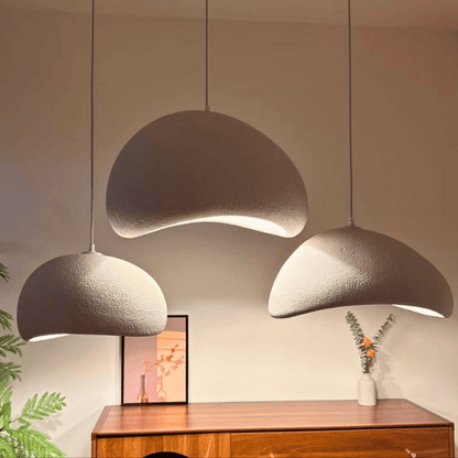 Three modern pendant lights hanging above a wooden cabinet with a plant and vase in the background.
