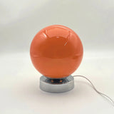 Orange spherical lamp with a silver base on a white background