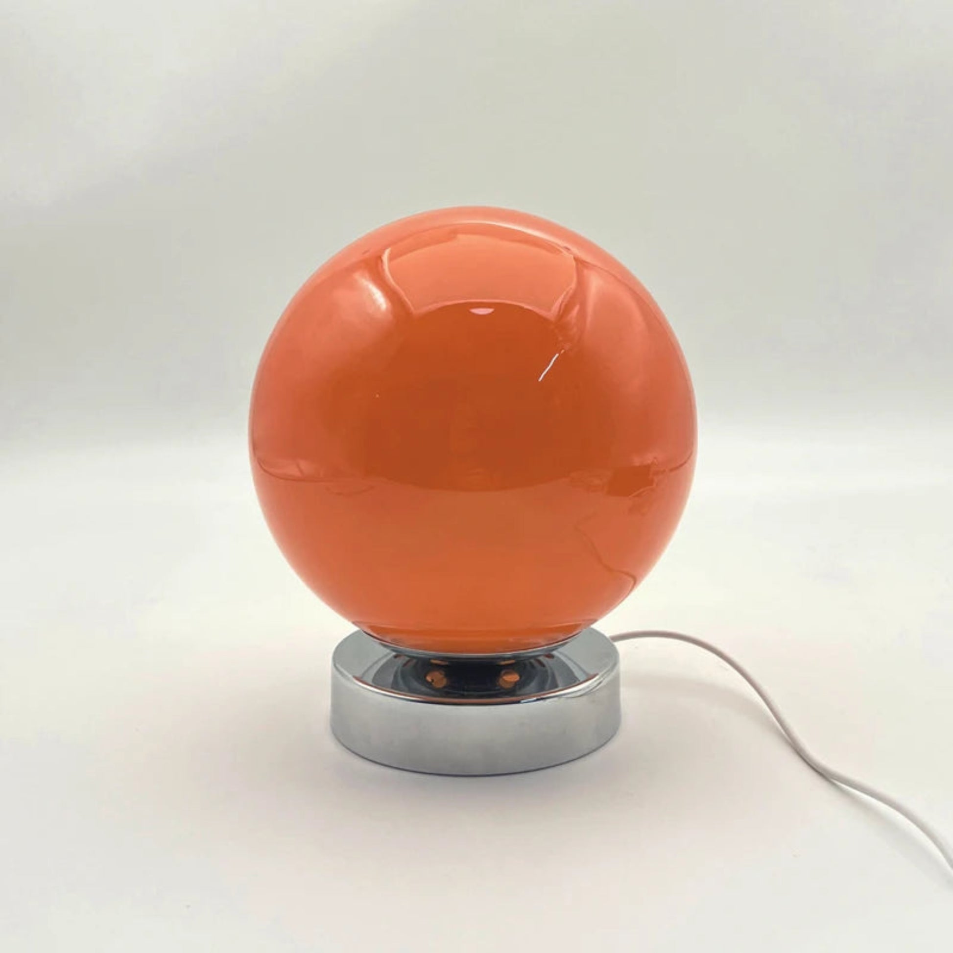 Orange spherical lamp with a silver base on a white background
