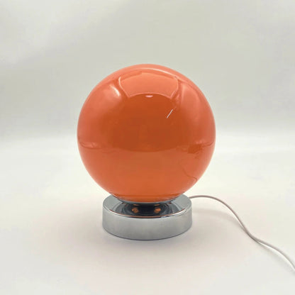Orange spherical lamp with a silver base on a white background