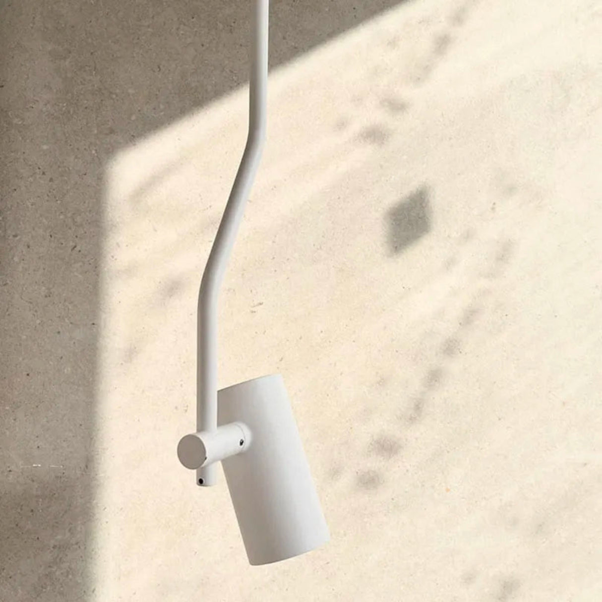 A minimalist white wall-mounted swing-arm pendant light with a cylindrical shade, shown against a textured beige wall with soft shadows.