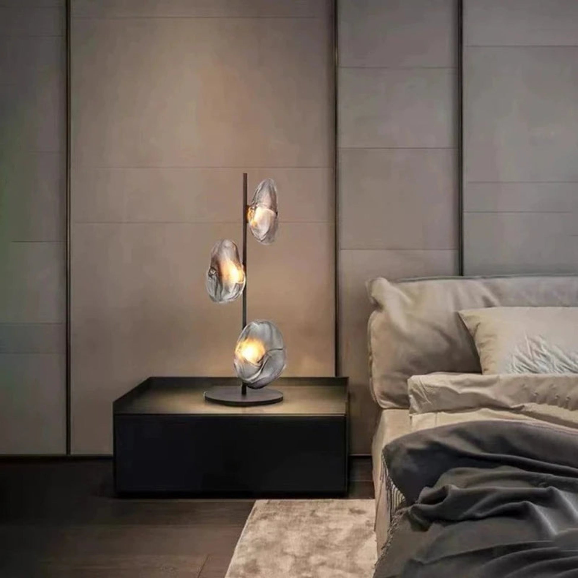 Modern bedroom with a stylish lamp on a nightstand and a bed in the background.