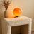 Orange spherical lamp on a textured surface with a vase of dried flowers.