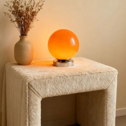 Orange spherical lamp on a textured surface with a vase of dried flowers.