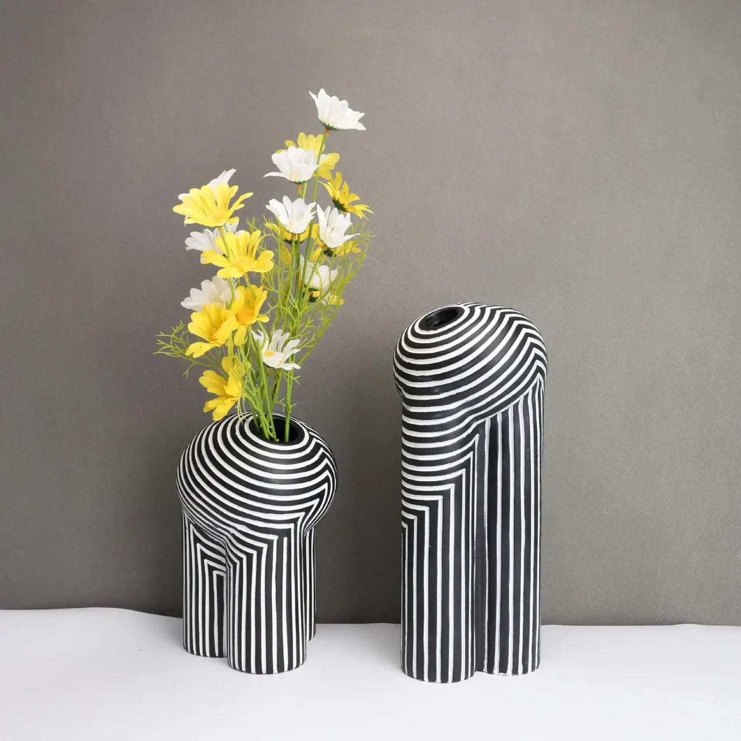 Two black and white striped vases with a bouquet of yellow and white flowers on a gray background.