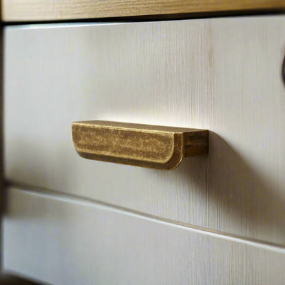 Close-up of a brass drawer handle on a wooden cabinet.