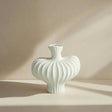 White textured vase on a light surface with a gray paneled wall background