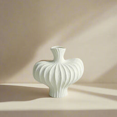 White textured vase on a light surface with a gray paneled wall background