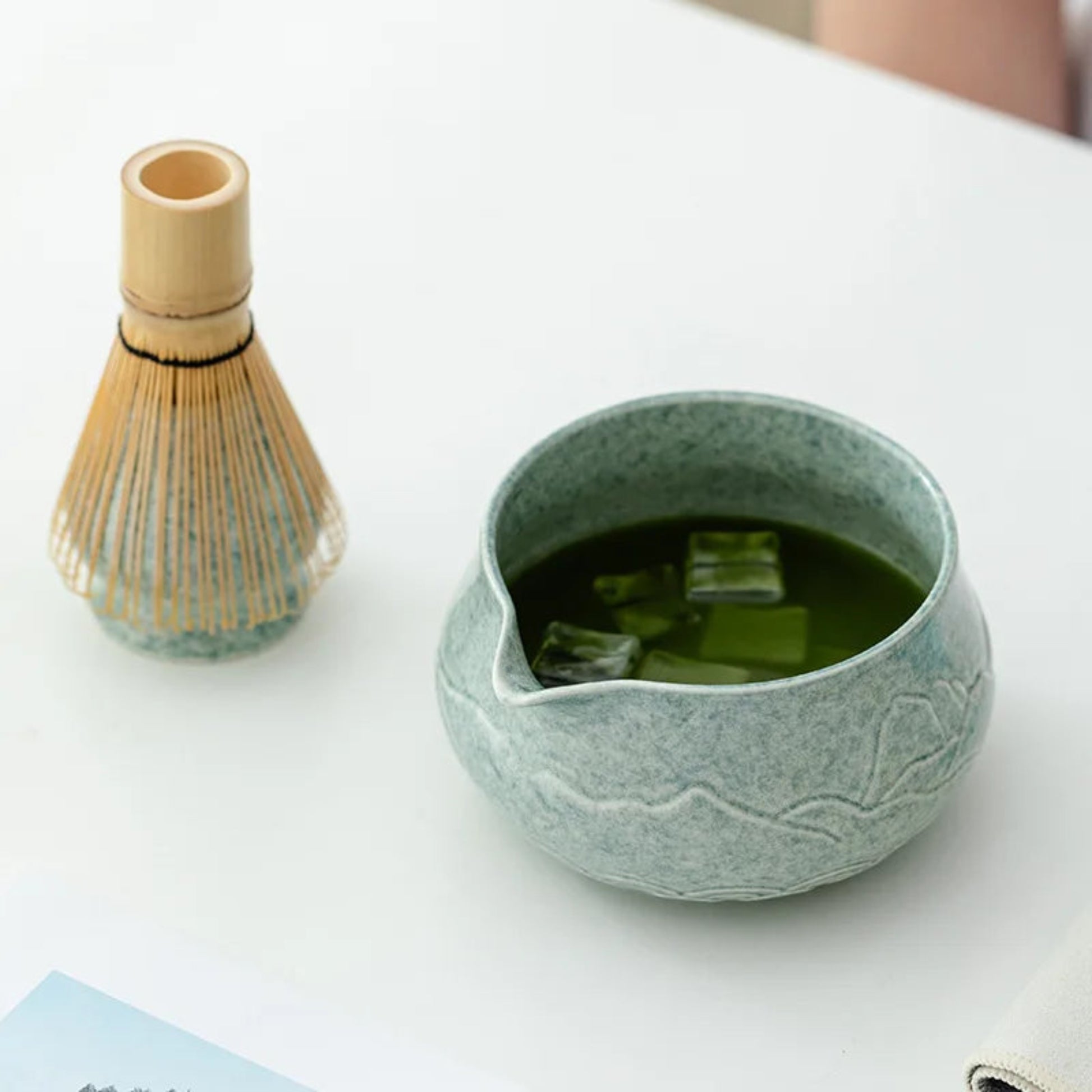 Green ceramic tea bowl with a bamboo whisk on a white surface