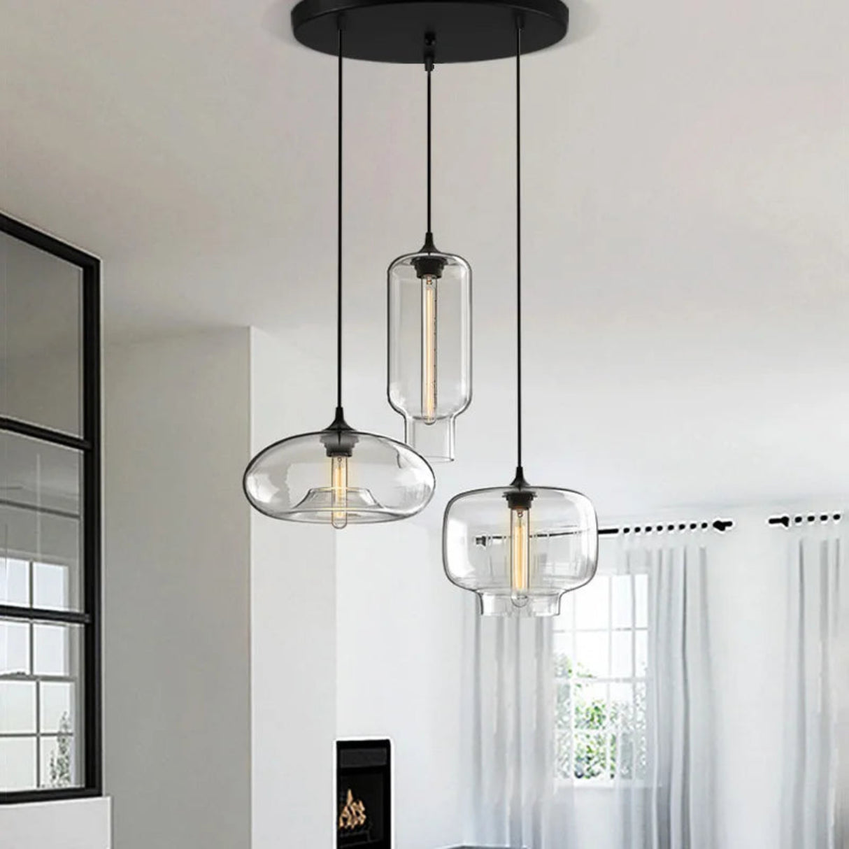 Three modern pendant lights with glass shades hanging in a room with a window and curtain.