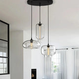 Three modern pendant lights with glass shades hanging in a room with a window and curtain.