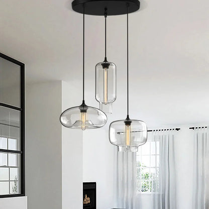 Three modern pendant lights with glass shades hanging in a room with a window and curtain.