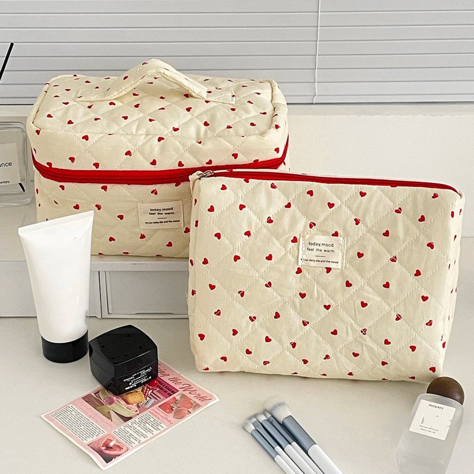 Two beige bags with red heart patterns on a white surface with stationery items.