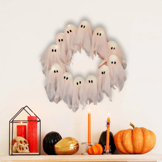 Halloween wreath with ghost decorations on a shelf with candles and pumpkins.