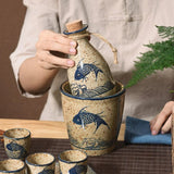 Ceramic bottle with cork stopper and blue fish design, held by a person with a plant in the background.
