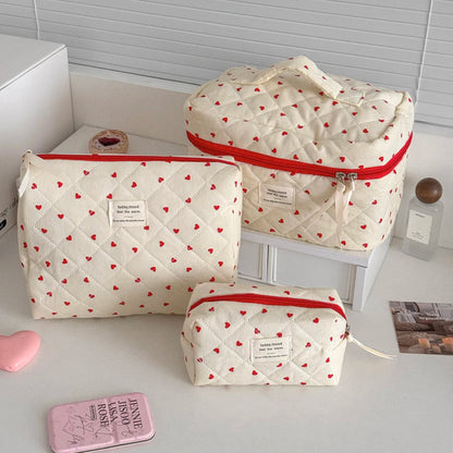Set of three white storage bags with red heart patterns on a white surface.