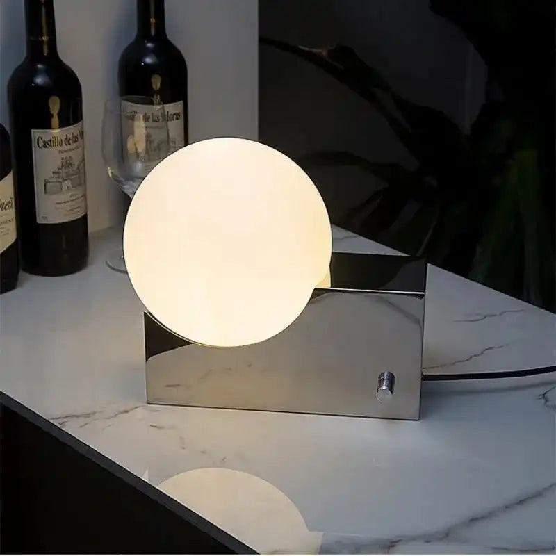 Modern LED desk lamp with dimmable glass ball and chrome base on a marble counter. Elegant lighting for home or bar settings.