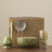 Tea-making set with green ceramic bowl, strainer, whisk, and glass on a beige background