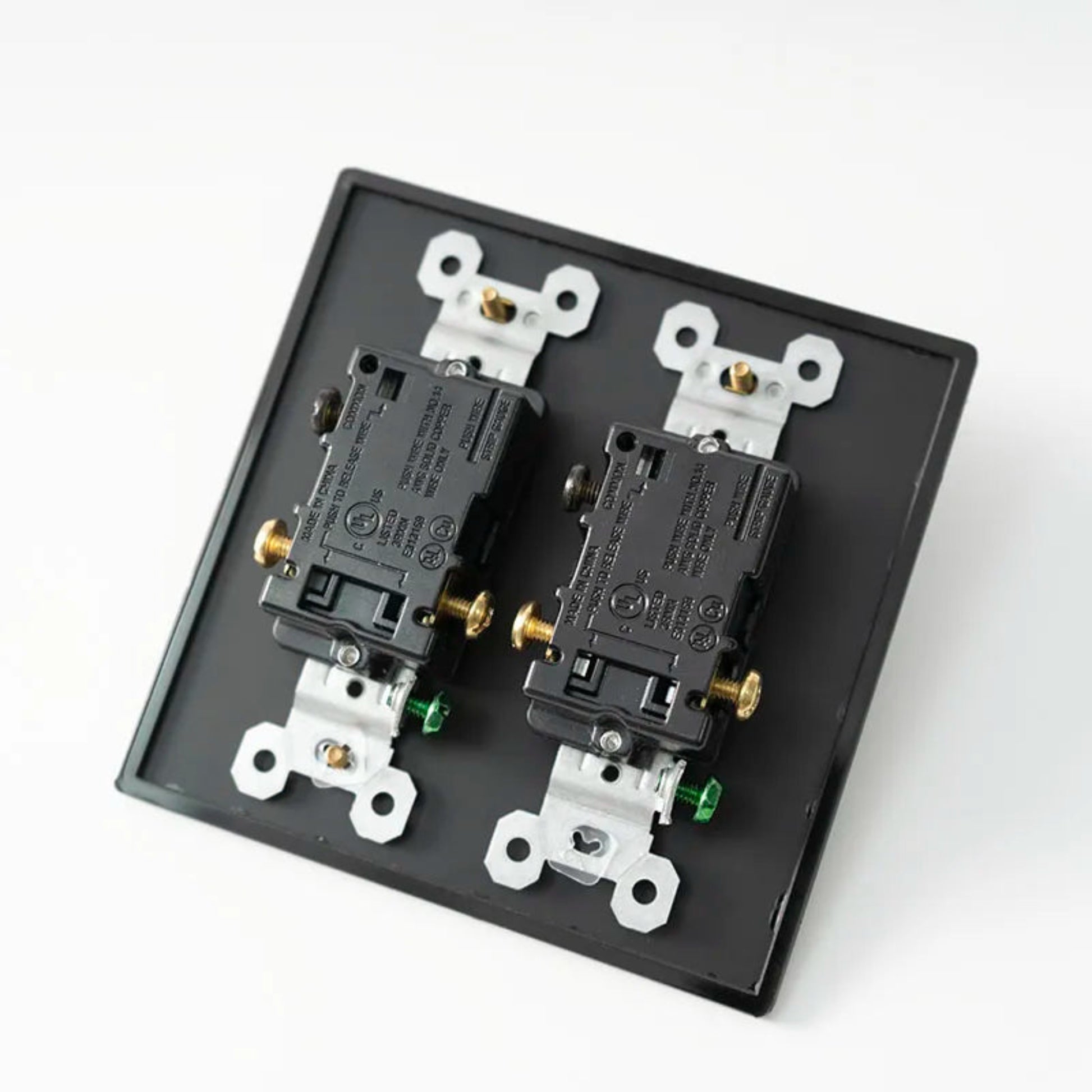 Two electrical outlets on a black faceplate with white and gold screws against a white background.