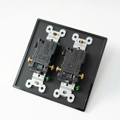 Two electrical outlets on a black faceplate with white and gold screws against a white background.