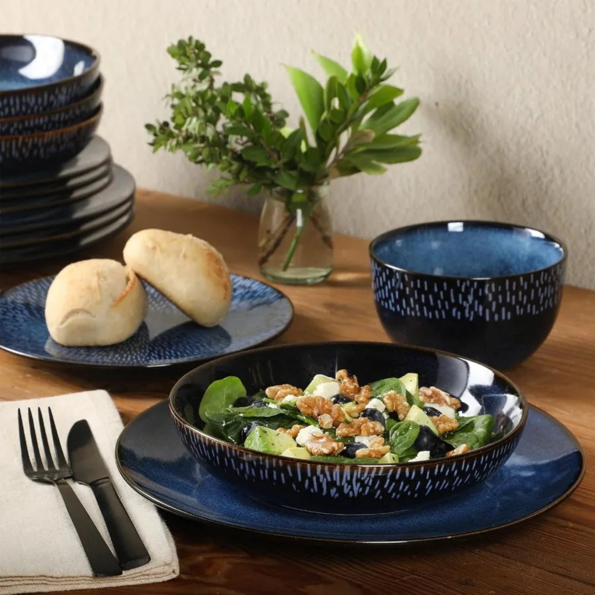 Blue ceramic tableware set with a salad bowl, plates, and bread on a wooden table.