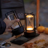 Hand holding a black lantern with another lantern on a table with pumpkins and leaves.