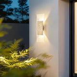Modern outdoor wall light fixture on a building exterior with plants in the foreground.