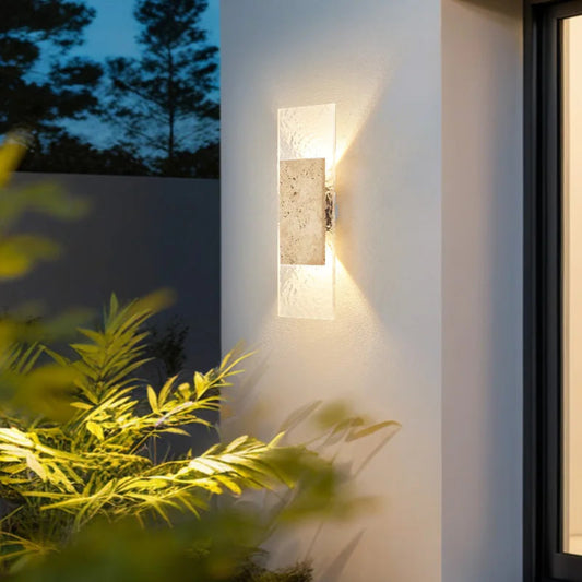 Modern outdoor wall light fixture on a building exterior with plants in the foreground.