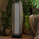 Decorative lamp with woven design in a room with plants and furniture.