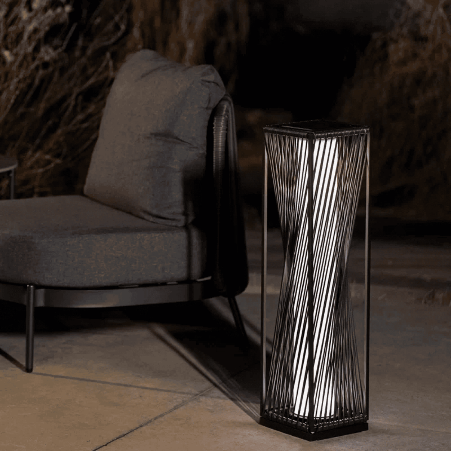 Decorative black pedestal with wavy design next to a gray cushioned chair in a dimly lit room.