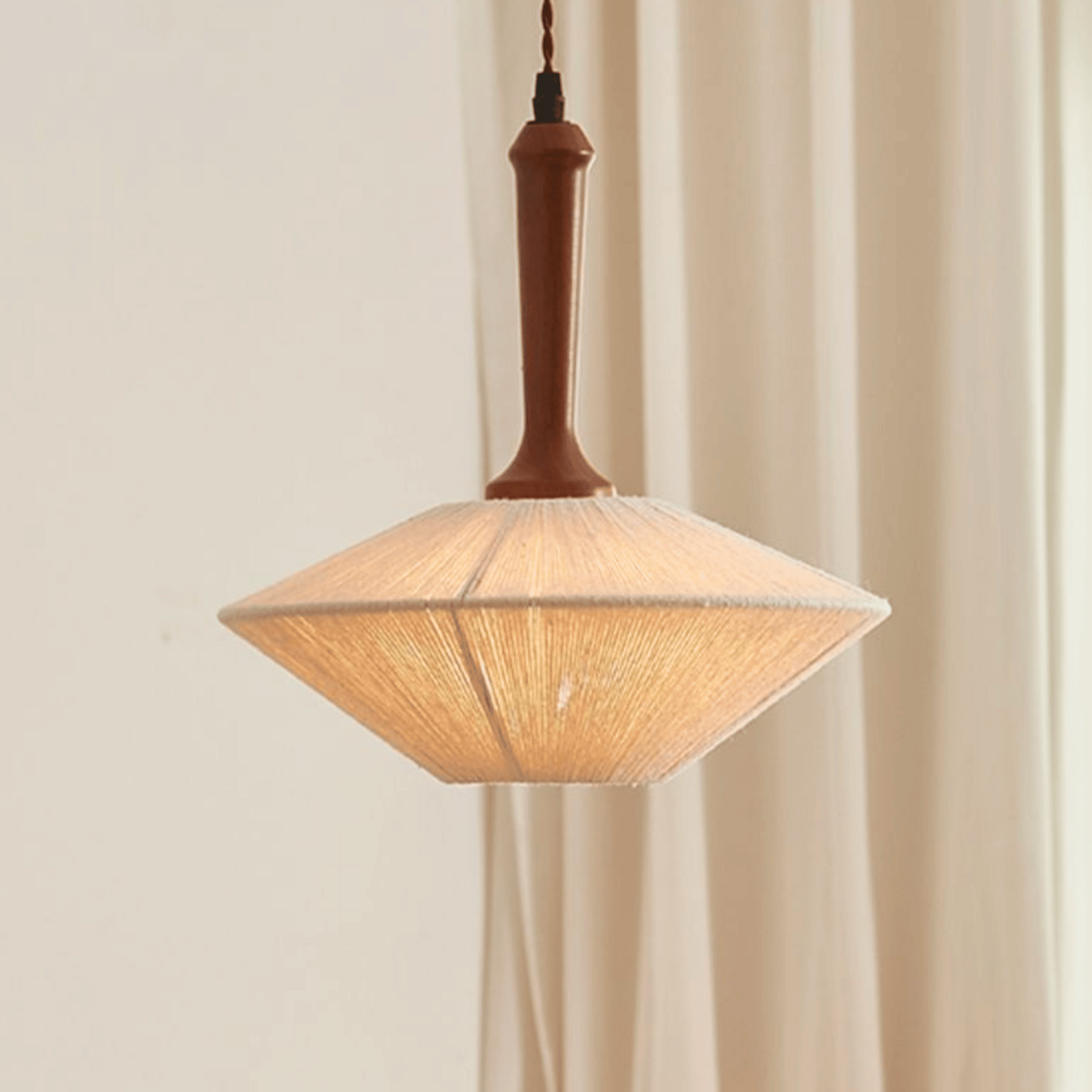 Pendant light with wooden fixture and woven shade against a beige curtain background