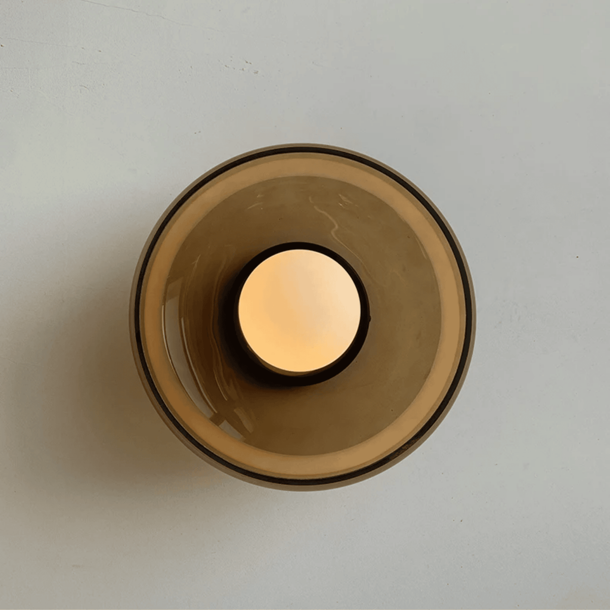 Glass candle holder with a lit candle on a light gray background