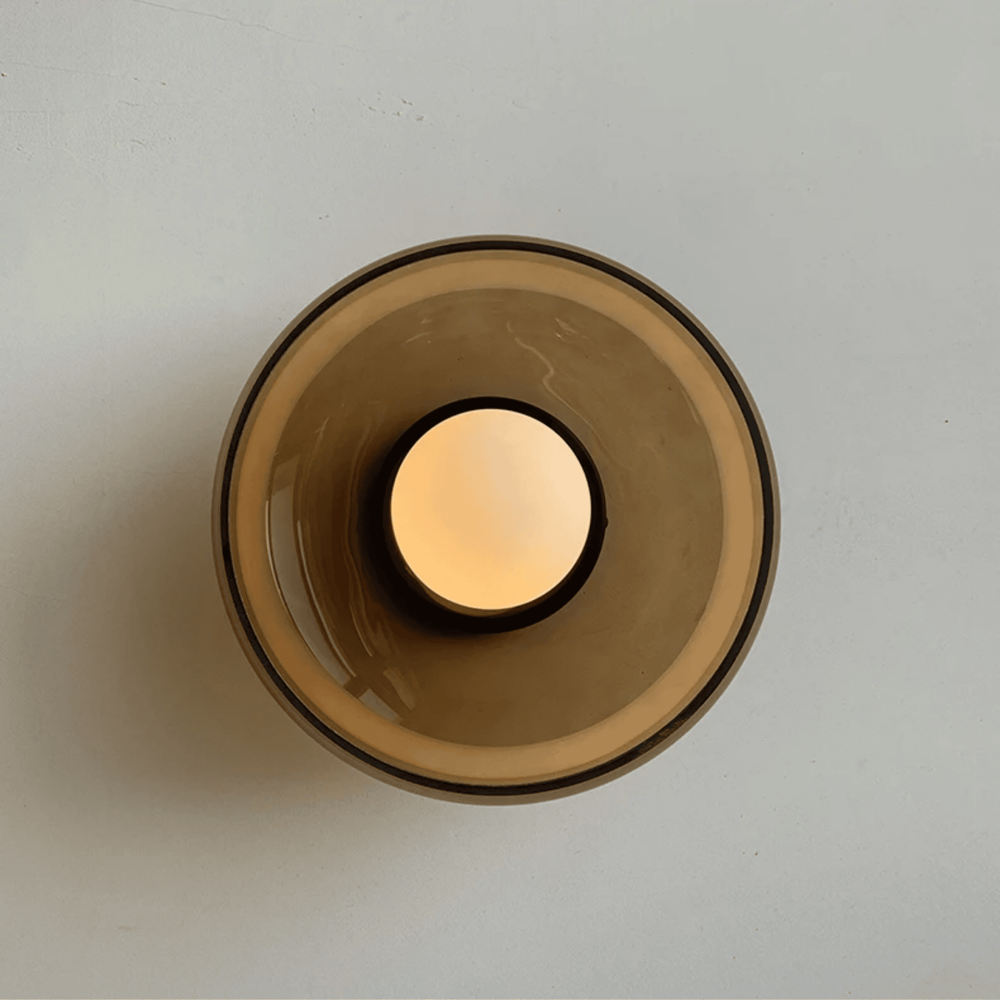 Glass candle holder with a lit candle on a light gray background