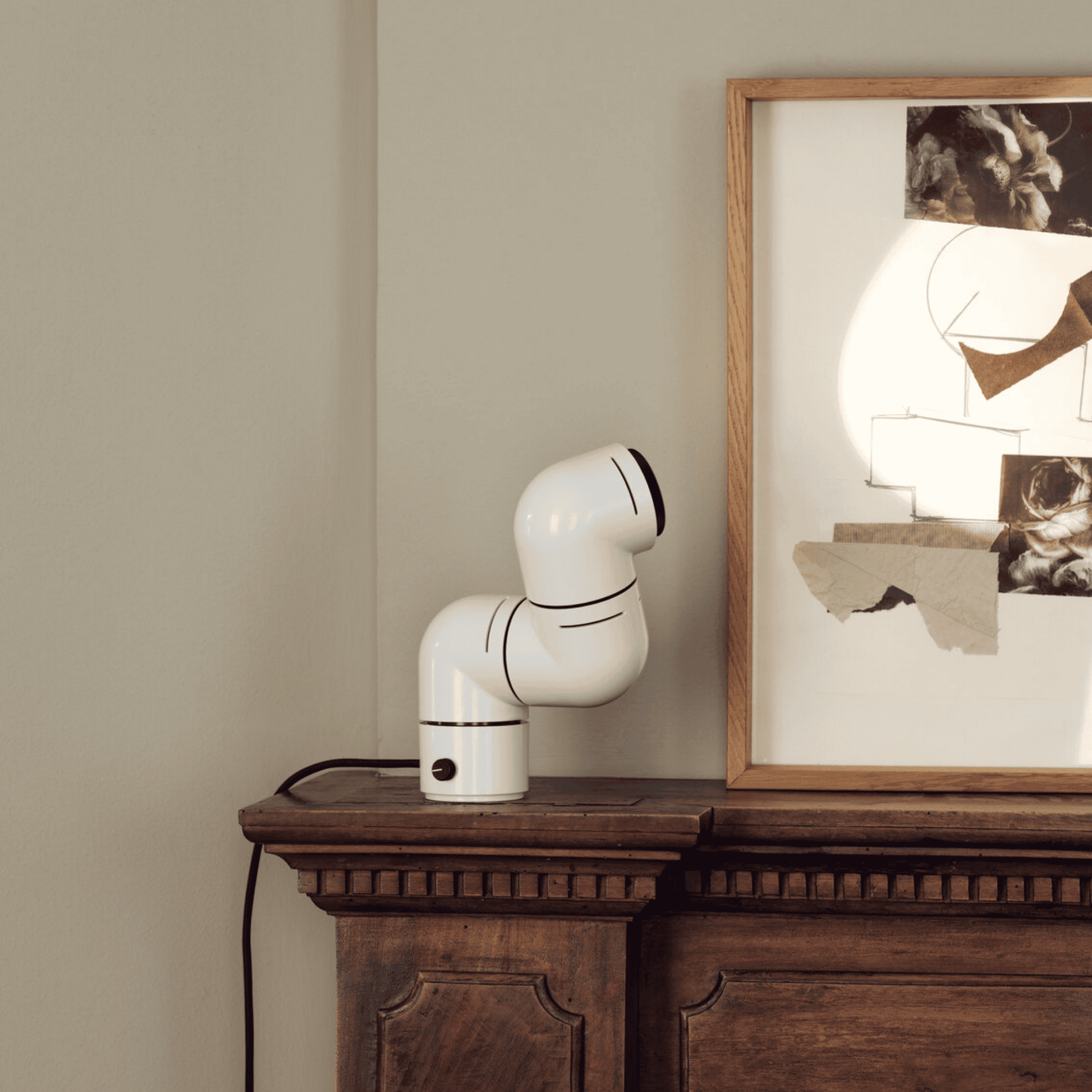 White robot-like device on a wooden surface with a framed picture in the background