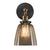 Vintage-style wall sconce with clear glass shade and brass fixture on a brown background