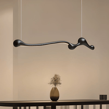 Modern black pendant light hanging above a table with a vase on a neutral background