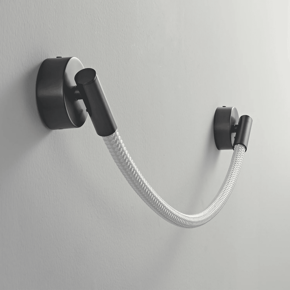 Black wall-mounted lamp with a flexible white hose on a gray background