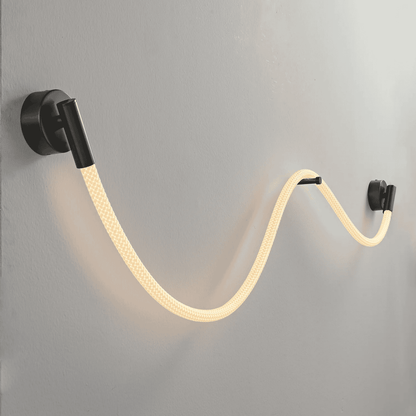 Wall-mounted light fixture with a flexible, illuminated cable on a gray wall.